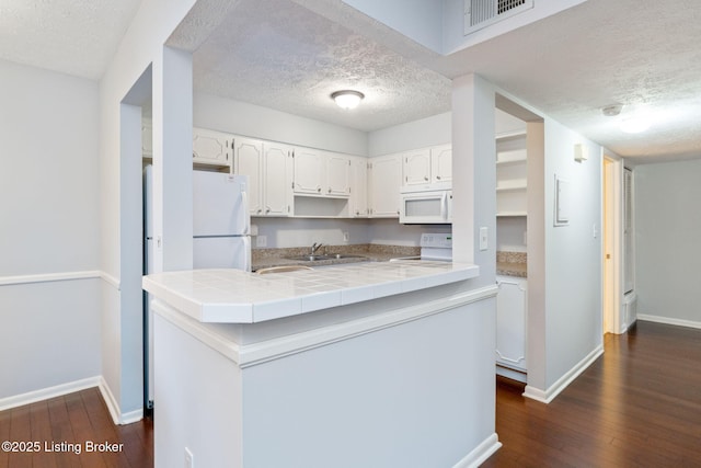 kitchen with sink, tile counters, kitchen peninsula, white appliances, and white cabinets