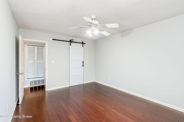 unfurnished bedroom with dark wood-type flooring, ceiling fan, a barn door, and a textured ceiling