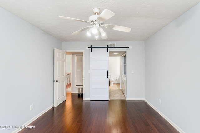 unfurnished bedroom with dark hardwood / wood-style floors, a barn door, and a textured ceiling