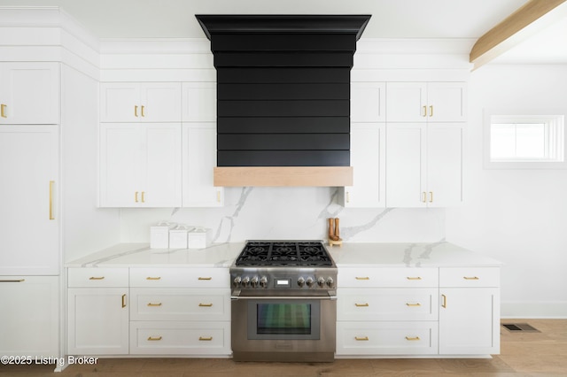 kitchen with stainless steel stove, tasteful backsplash, white cabinets, light stone counters, and light wood-type flooring