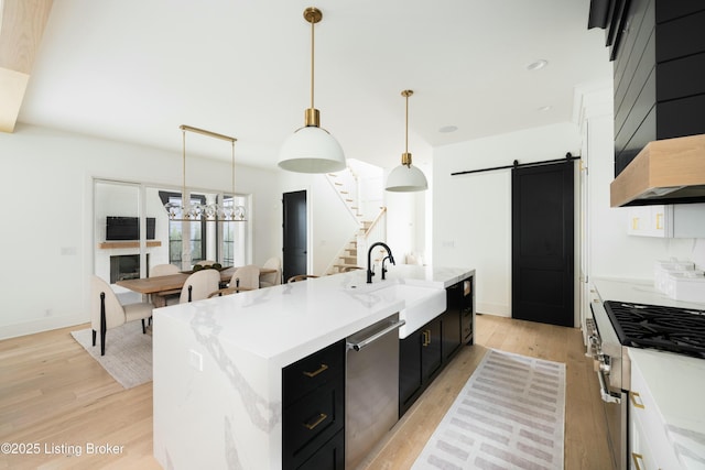 kitchen featuring hanging light fixtures, a barn door, sink, and a center island with sink