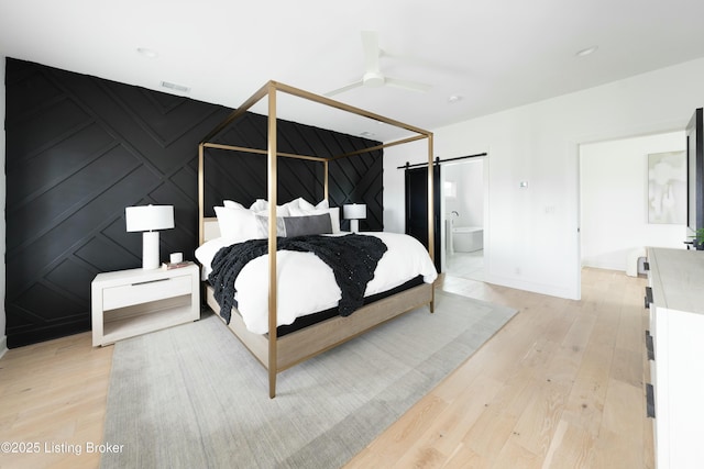 bedroom featuring ceiling fan, a barn door, light wood-type flooring, and ensuite bath