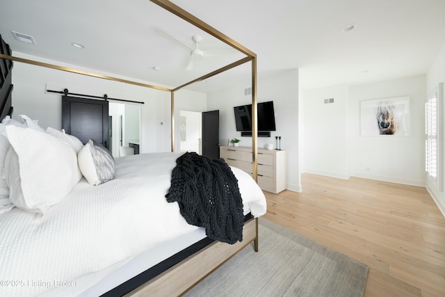 bedroom with ceiling fan, a barn door, and light wood-type flooring