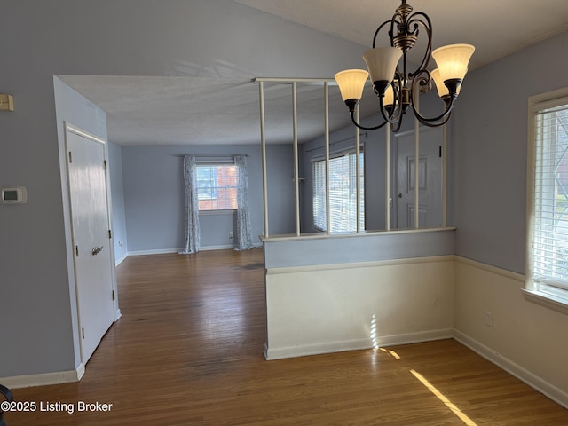 unfurnished dining area with dark wood-type flooring, lofted ceiling, and an inviting chandelier