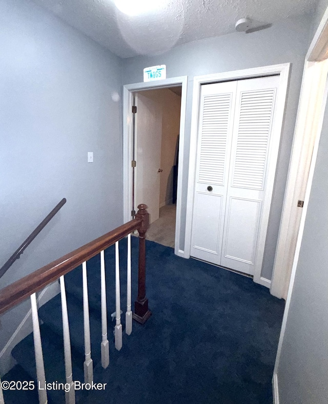 hallway with a textured ceiling and dark colored carpet