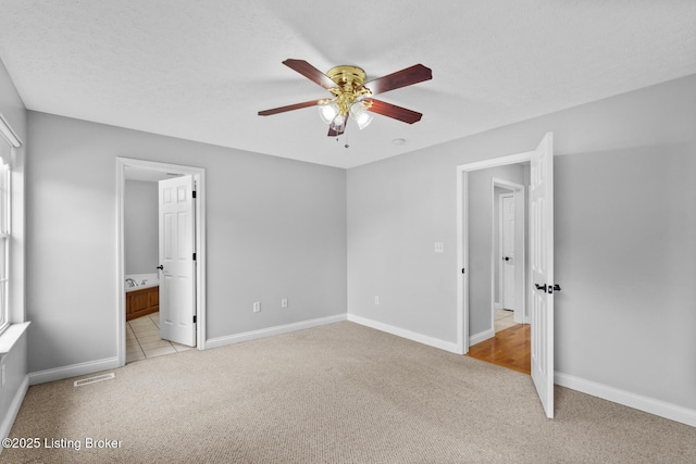 unfurnished bedroom featuring ensuite bathroom, light carpet, ceiling fan, and a textured ceiling