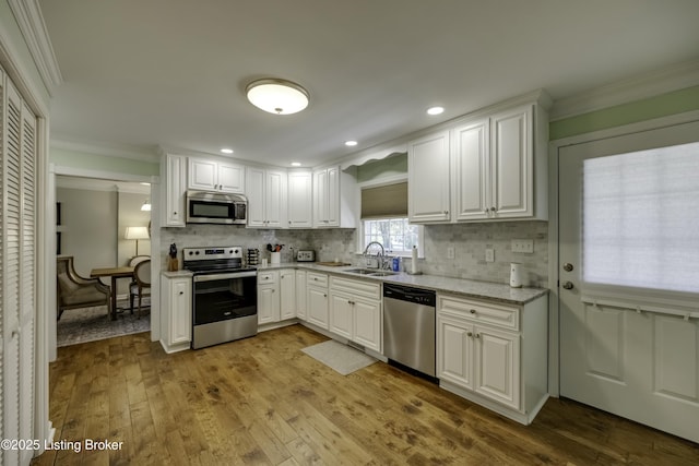 kitchen featuring appliances with stainless steel finishes, white cabinetry, sink, decorative backsplash, and crown molding