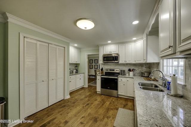 kitchen with appliances with stainless steel finishes, sink, white cabinets, ornamental molding, and light stone counters