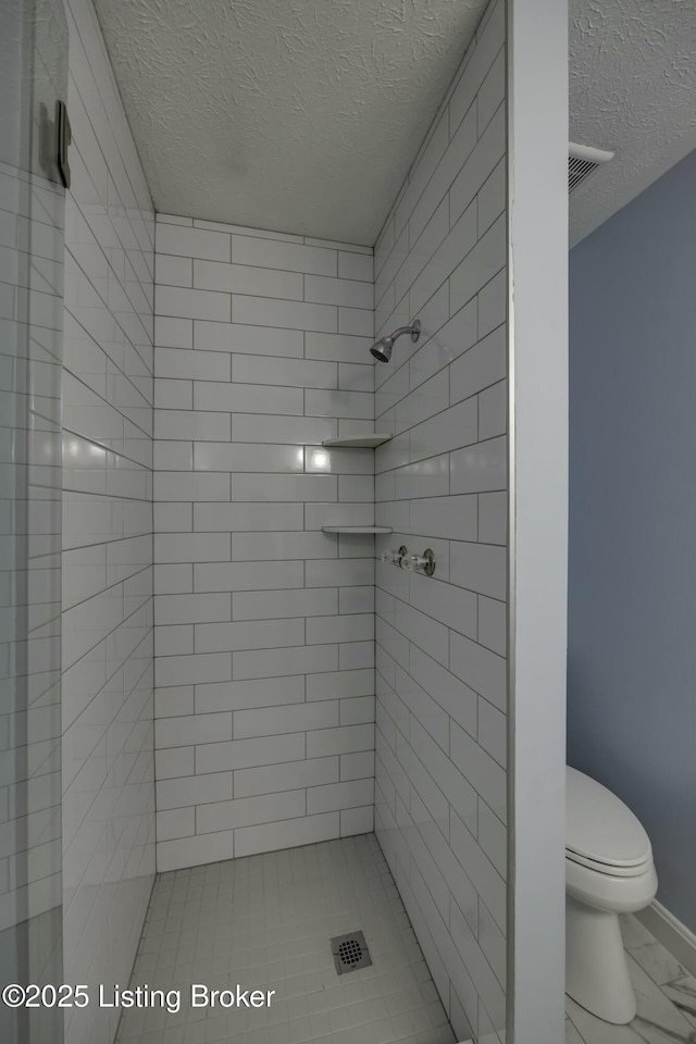 bathroom with a tile shower, a textured ceiling, and toilet