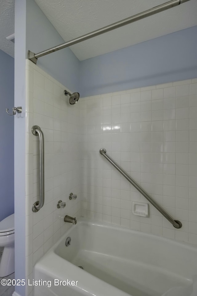 bathroom featuring tiled shower / bath, toilet, and a textured ceiling