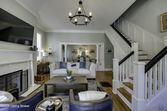 living room featuring crown molding, wood-type flooring, a fireplace, and an inviting chandelier