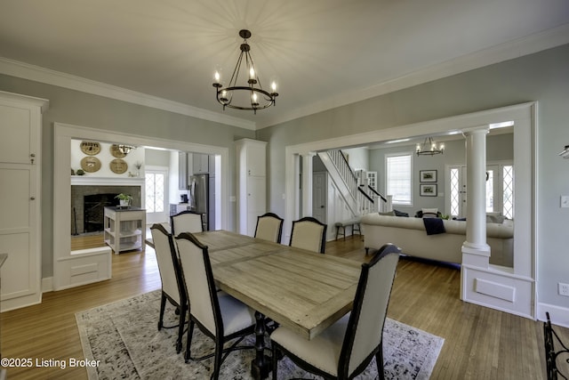 dining area with ornate columns, wood-type flooring, crown molding, and an inviting chandelier