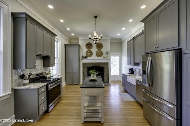 kitchen with gray cabinets, appliances with stainless steel finishes, ornamental molding, decorative light fixtures, and light wood-type flooring