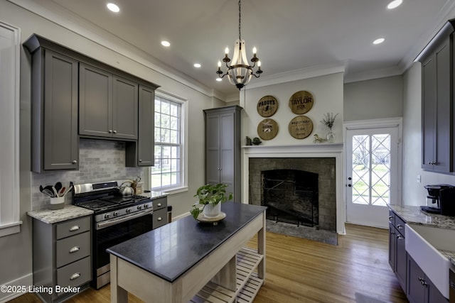 kitchen with crown molding, gray cabinets, dark stone countertops, hanging light fixtures, and stainless steel range with gas stovetop