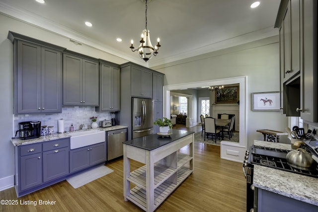 kitchen with sink, light wood-type flooring, ornamental molding, pendant lighting, and stainless steel appliances