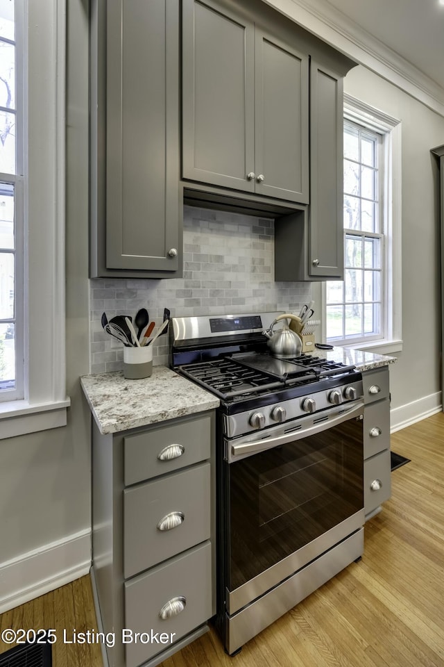 kitchen featuring gas range, backsplash, light stone countertops, and gray cabinetry