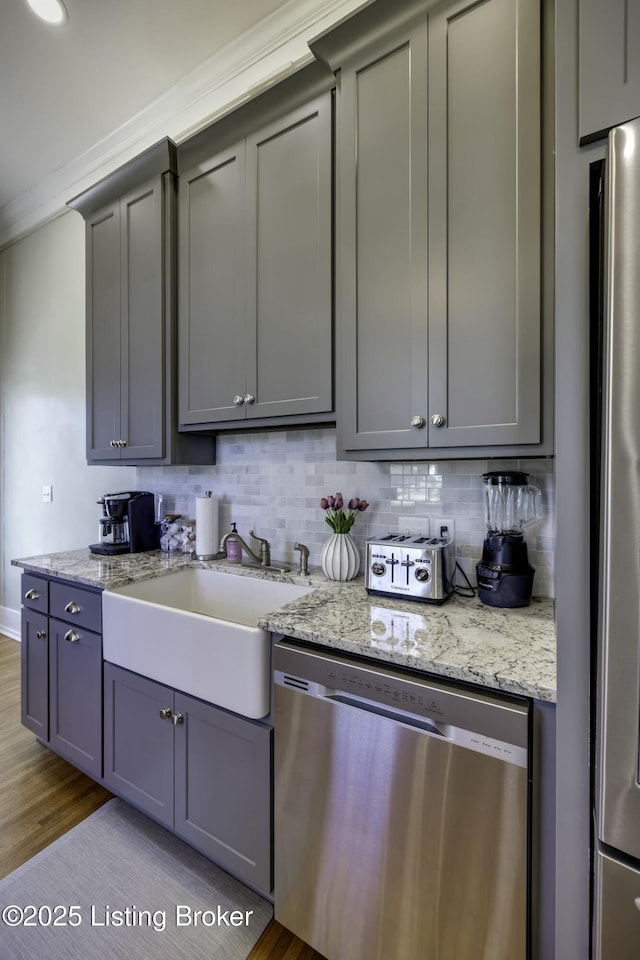 kitchen featuring tasteful backsplash, sink, gray cabinetry, light stone counters, and stainless steel appliances