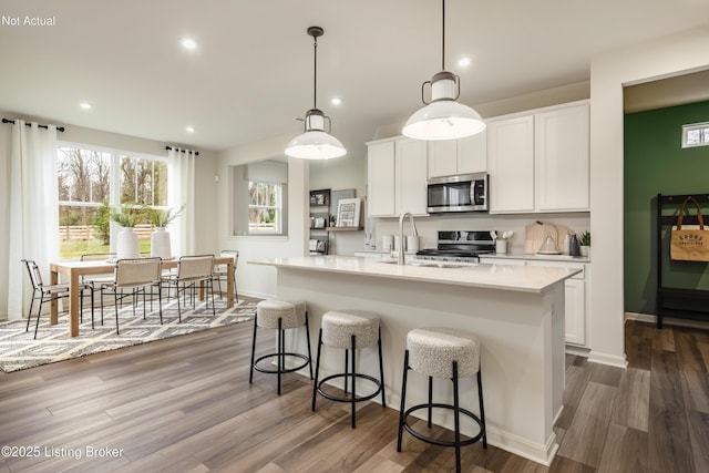 kitchen featuring sink, hanging light fixtures, a center island with sink, white cabinets, and stove