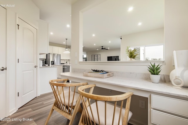 kitchen featuring a kitchen bar, light stone counters, decorative light fixtures, stainless steel appliances, and white cabinets