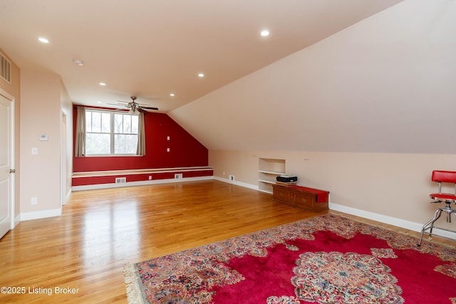 additional living space with built in shelves, vaulted ceiling, ceiling fan, and hardwood / wood-style flooring