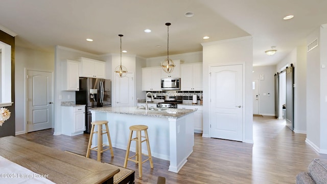 kitchen with white cabinets, a barn door, stainless steel appliances, light stone countertops, and a center island with sink