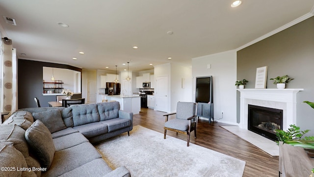 living room with hardwood / wood-style floors, crown molding, a tile fireplace, and sink