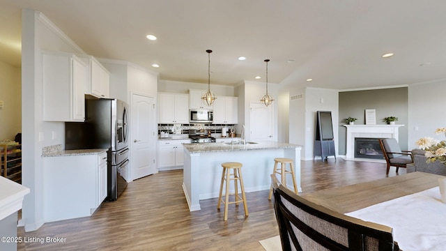 kitchen featuring an island with sink, sink, white cabinets, light stone counters, and stainless steel appliances