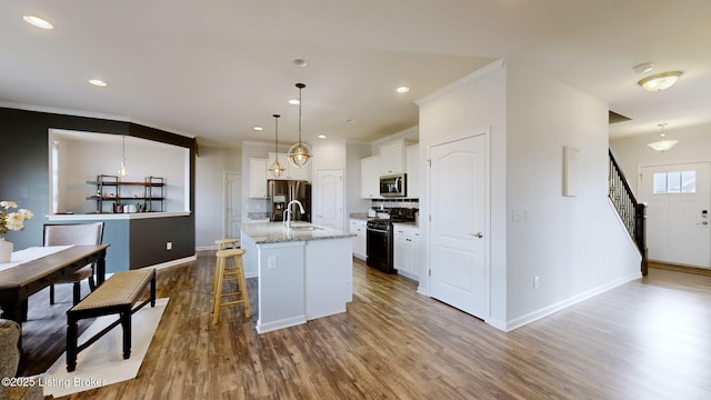 kitchen with appliances with stainless steel finishes, white cabinetry, hanging light fixtures, light stone counters, and an island with sink