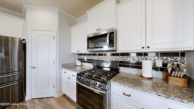 kitchen with ornamental molding, appliances with stainless steel finishes, white cabinets, and light stone counters