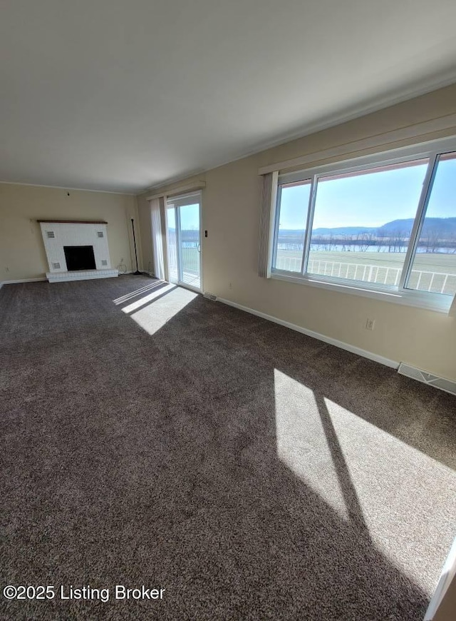 unfurnished living room with a fireplace, a water and mountain view, plenty of natural light, and carpet