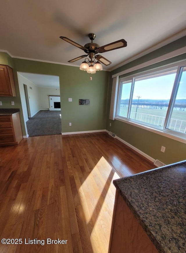 unfurnished living room with hardwood / wood-style flooring, ornamental molding, ceiling fan, and a water view