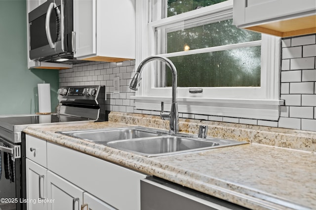 kitchen with decorative backsplash, white cabinets, a sink, stainless steel appliances, and light countertops