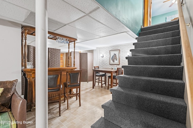 stairs featuring a paneled ceiling and a dry bar