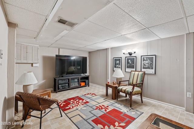 living room featuring baseboards, visible vents, a decorative wall, and a drop ceiling