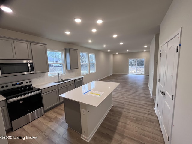 kitchen featuring sink, light hardwood / wood-style flooring, gray cabinetry, stainless steel appliances, and a kitchen island