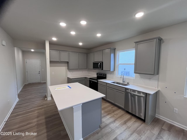 kitchen with sink, gray cabinets, appliances with stainless steel finishes, a kitchen island, and light wood-type flooring