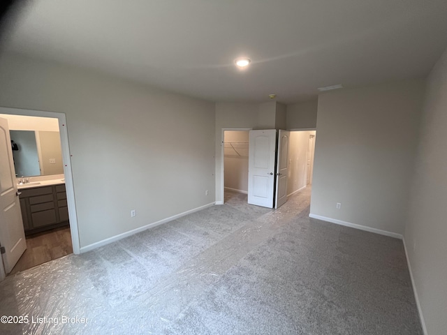 unfurnished bedroom featuring sink, ensuite bathroom, light carpet, a walk in closet, and a closet