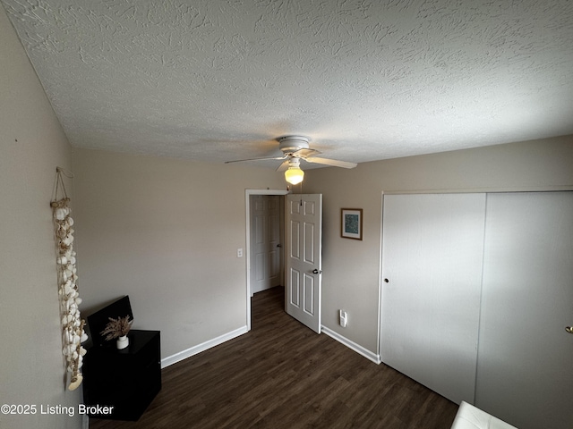 unfurnished bedroom featuring dark wood-type flooring, a textured ceiling, ceiling fan, and a closet