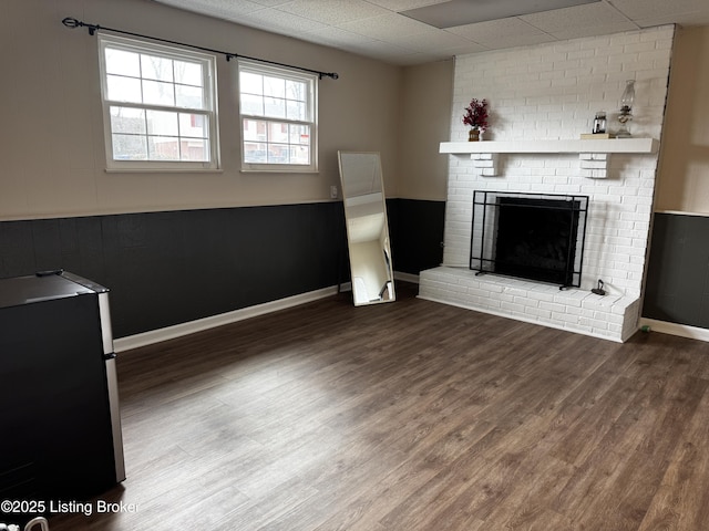 unfurnished living room with hardwood / wood-style flooring, a paneled ceiling, and a brick fireplace