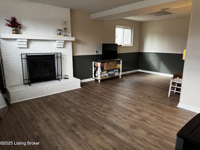 unfurnished living room featuring dark wood-type flooring, a paneled ceiling, and a brick fireplace