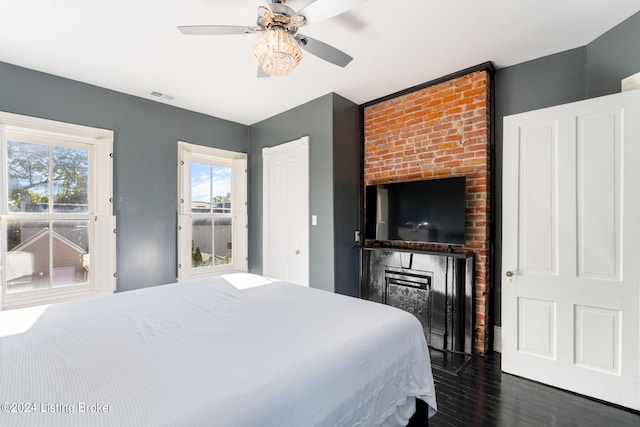 bedroom featuring dark wood-type flooring, ceiling fan, and a fireplace