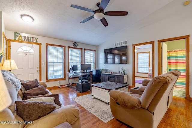 living room with lofted ceiling, ceiling fan, light hardwood / wood-style flooring, and a textured ceiling