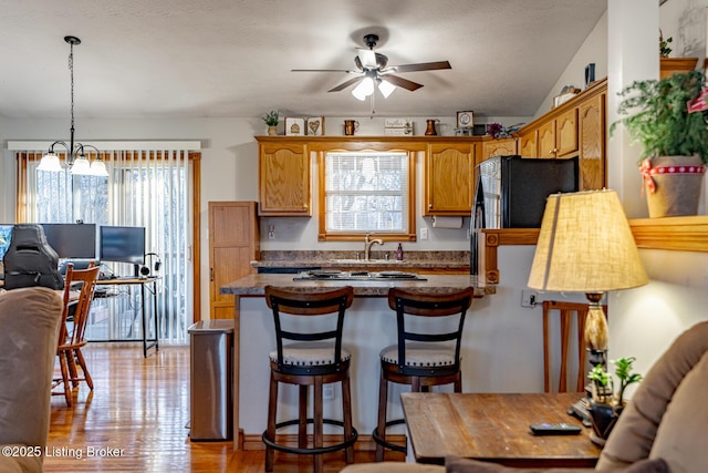 kitchen with a kitchen bar, stainless steel gas cooktop, light hardwood / wood-style floors, pendant lighting, and ceiling fan with notable chandelier