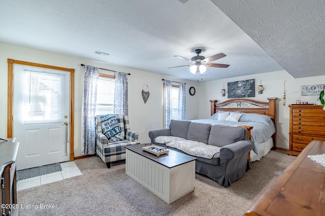 bedroom with ceiling fan, light colored carpet, and a textured ceiling