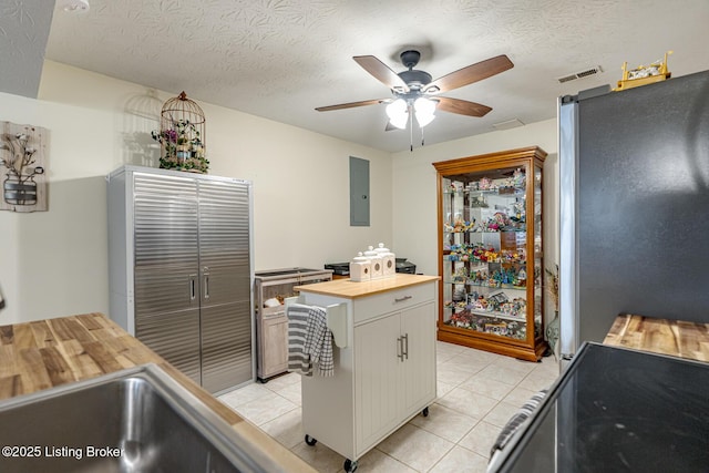 kitchen featuring light tile patterned flooring, butcher block countertops, stainless steel fridge, electric panel, and white cabinets