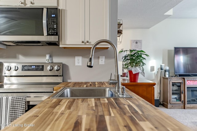 kitchen with white cabinetry, butcher block countertops, sink, and appliances with stainless steel finishes