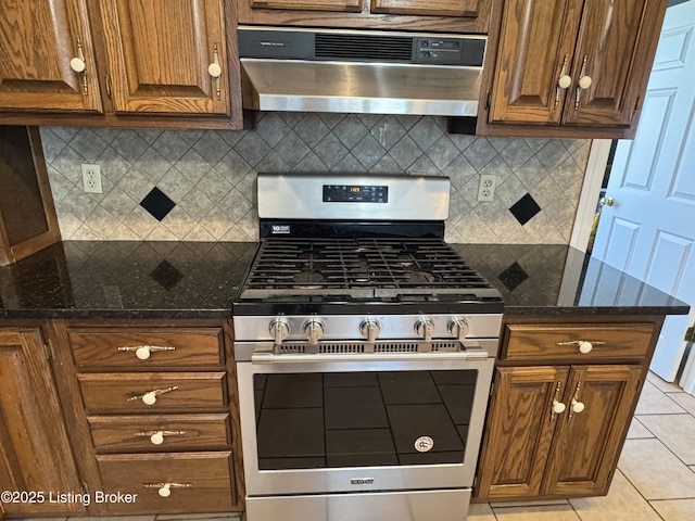 kitchen with light tile patterned floors, tasteful backsplash, gas stove, exhaust hood, and dark stone counters