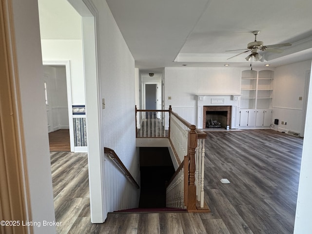 unfurnished living room featuring dark hardwood / wood-style flooring, a tray ceiling, built in features, and ceiling fan