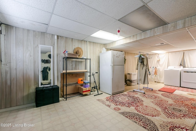 finished basement with separate washer and dryer, wood walls, freestanding refrigerator, and tile patterned floors