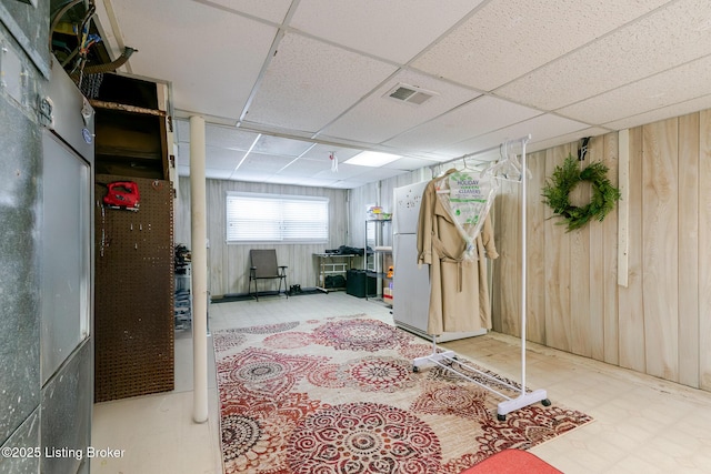 below grade area with a paneled ceiling, visible vents, wooden walls, and tile patterned floors